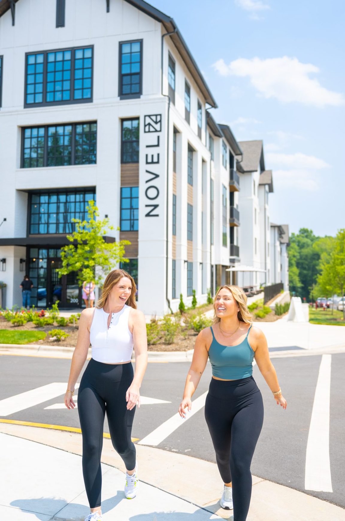 Two women walking together outside a modern apartment building on a sunny day