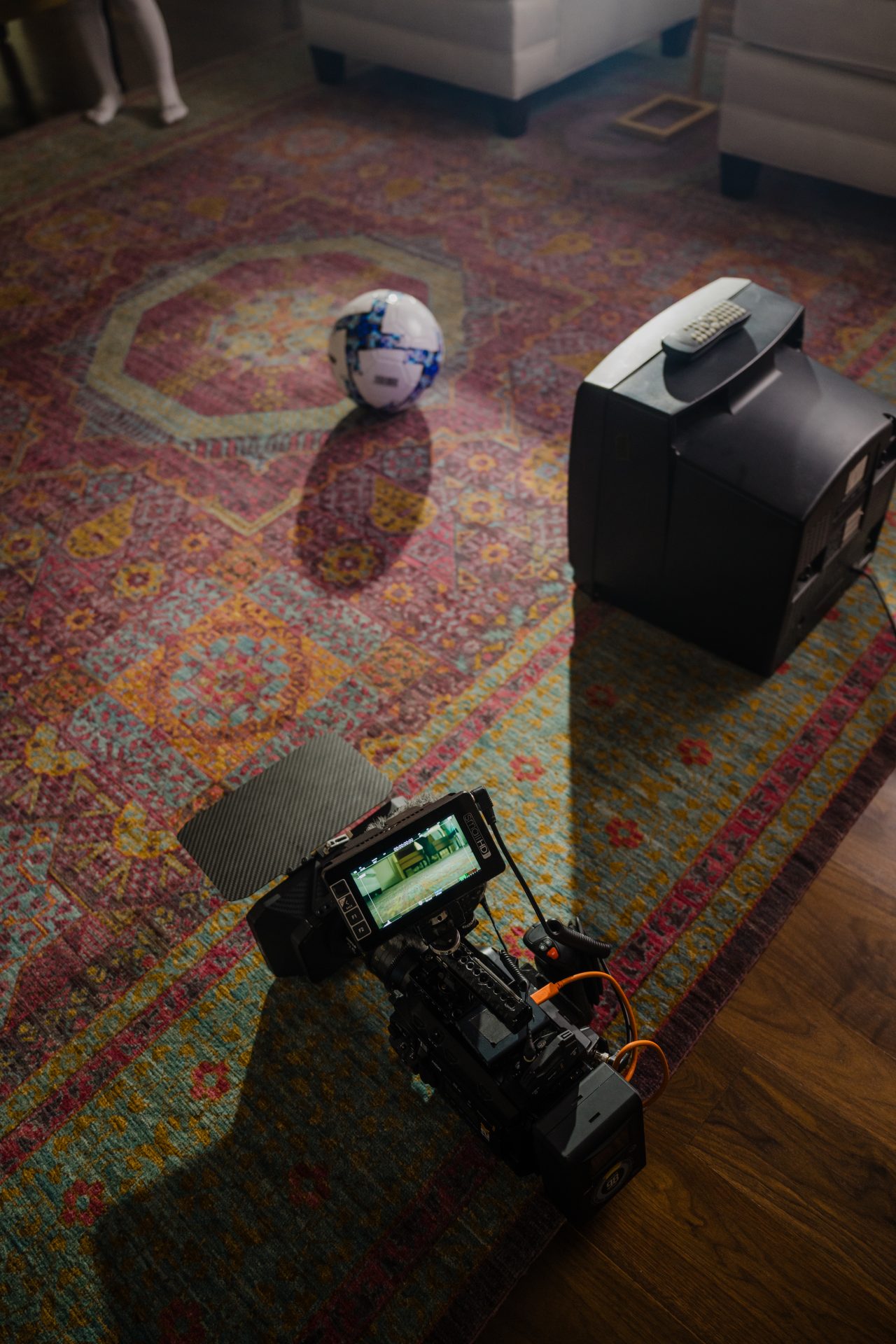 Behind-the-scenes photo of a camera rig and crew member filming a colorful patterned rug on location for a Rugs.com brand production