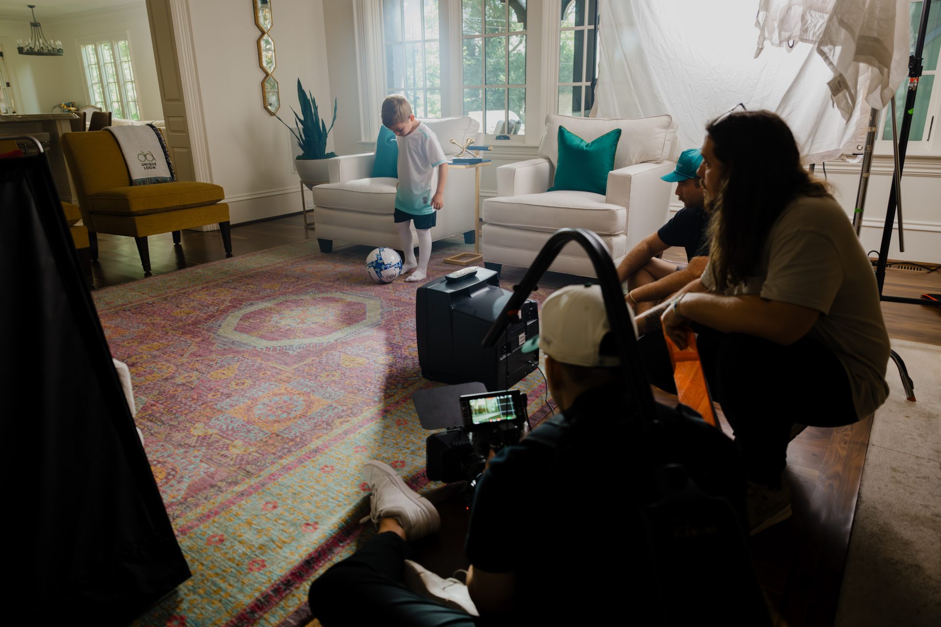 Behind-the-scenes video production shoot inside a furnished living room with camera crew and talent
