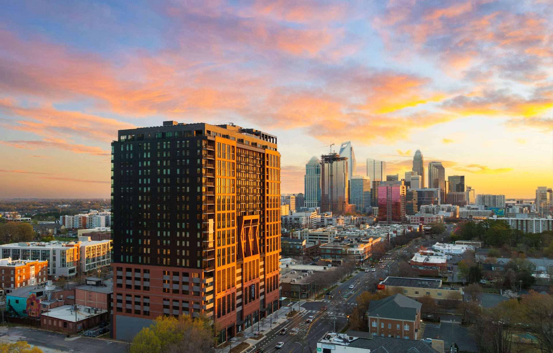 Dramatic sunset skyline with a modern high-rise building glowing against vibrant orange and purple clouds for Greystar real estate video content
