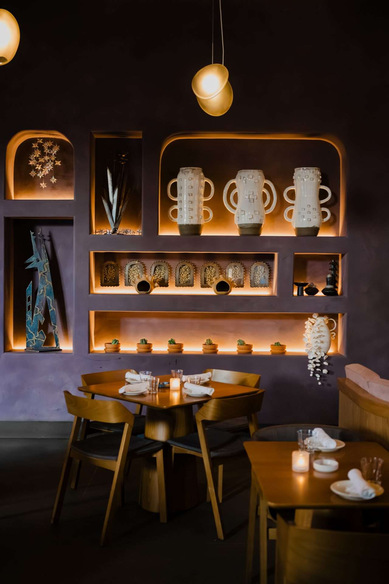 Warmly lit upscale restaurant interior with wooden shelves displaying cups and mugs, pendant lighting, and booth seating for an editorial brand photography shoot